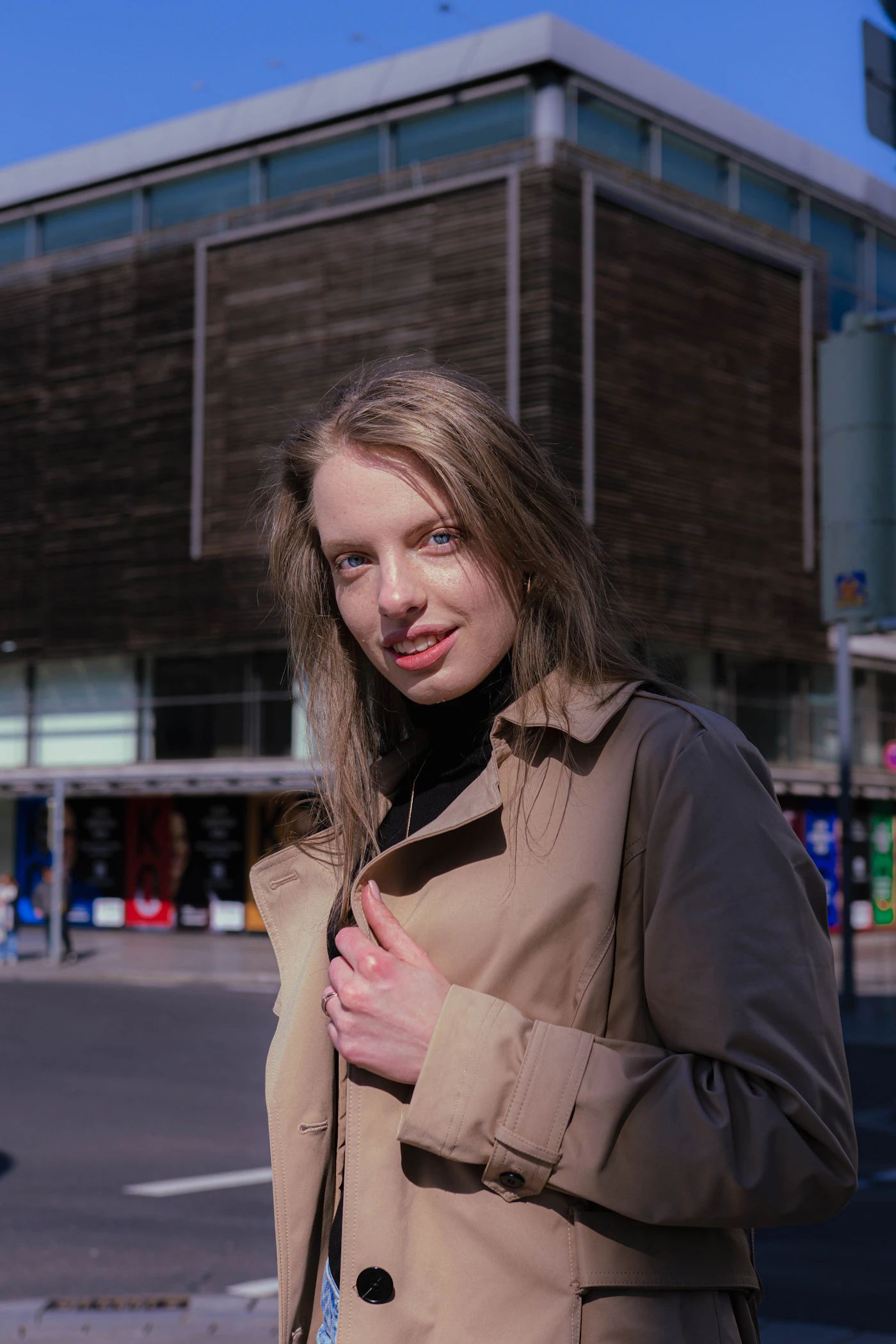 A young woman in a trench coat smiles outdoors
