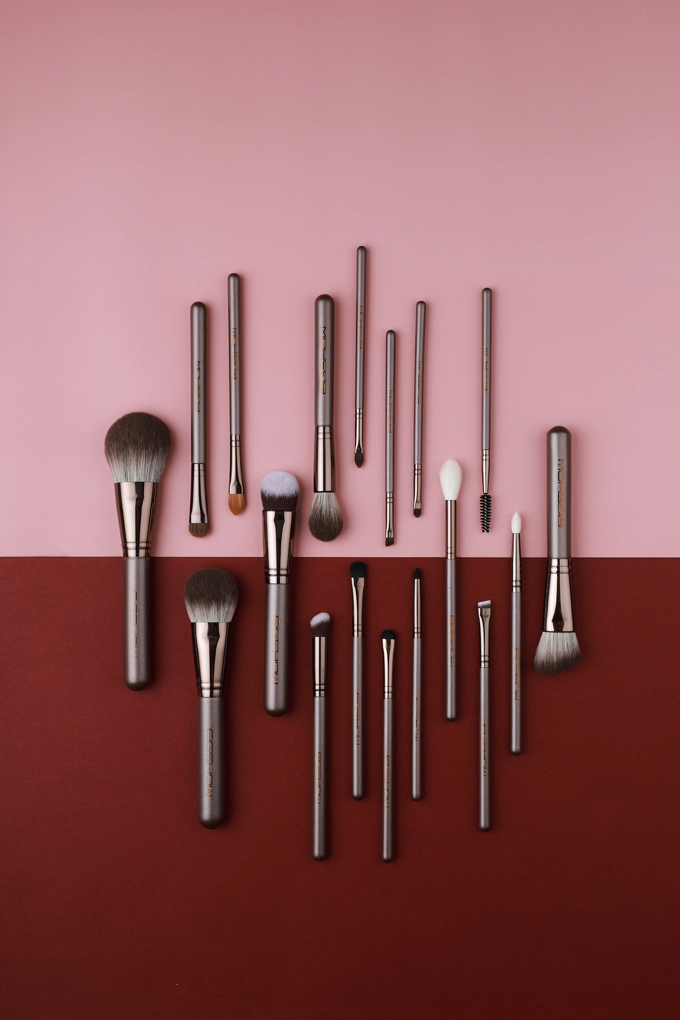 A collection of makeup brushes on a pink and red background